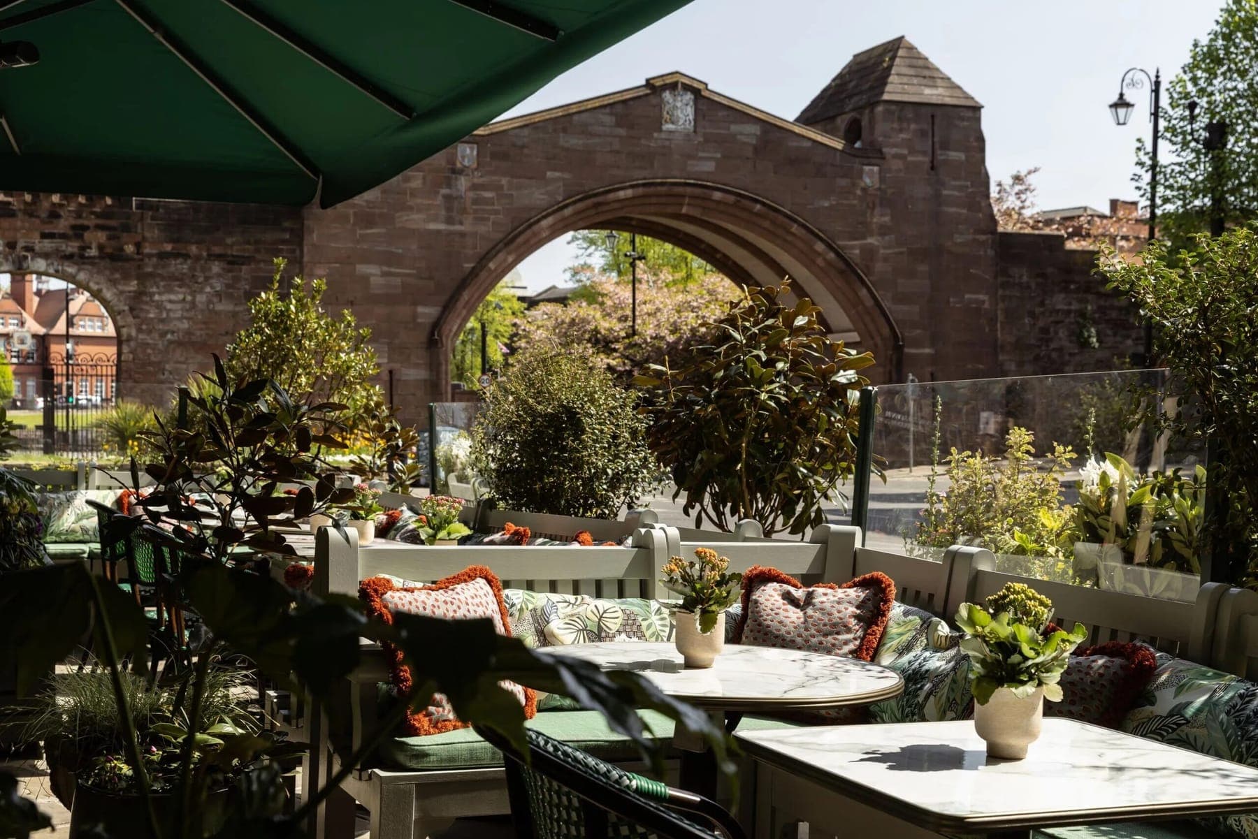 The outdoor dining terrace at The Ivy Brasserie Chester beneath a historic stone arch.